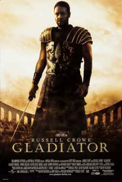 A man standing at the center of the image is wearing armor and is holding a sword in his right hand. In the background is the top of the Colosseum with a barely visible crowd standing in it. The poster includes the film's title and credits.