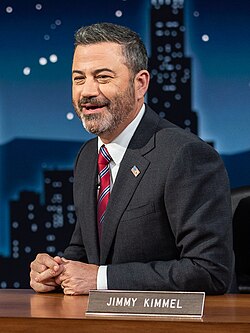 Photo of Kimmel smiling at his late-show desk