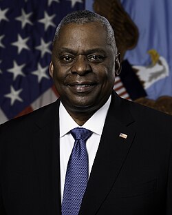 Former United States Secretary of Defense Lloyd Austin in his official portrait, taken in 2023. He is standing in front of a United States flag and a Department of Defense flag. He is wearing a black suit and a blue tie.