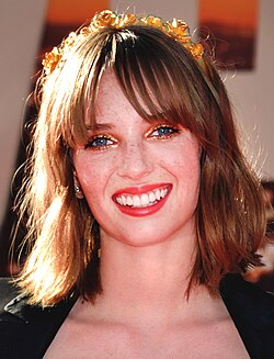 A smiling woman (Maya Hawke) with a bob haircut and flower crown