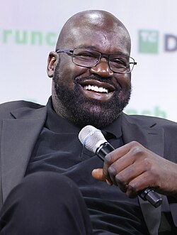 Head and shoulders photograph of O'Neal smiling and holding a microphone
