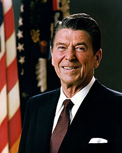 White House portrait of Reagan smiling in front of the US and US president flags, wearing a dark blue suit jacket with a white shirt and burgundy necktie.