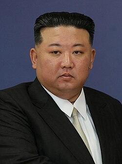 Photograph of Kim wearing a black suit jacket, a white shirt, and a white cream necktie.
