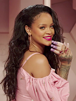 Rihanna smiling, holding three Fenty products