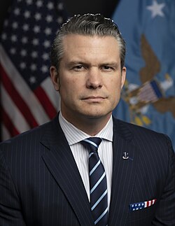 United States Secretary of Defense Pete Hegseth in his official portrait. He is wearing a dark navy blue suit and tie, with American and Department of Defense flags behind him.