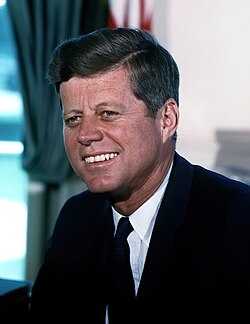 President Kennedy smiling and sitting in the Oval Office