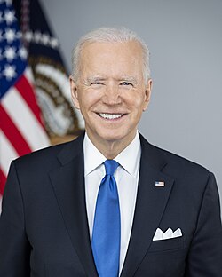 Official presidential portrait of Biden smiling, wearing a navy blue suit jacket with an American flag lapel pin, white shirt, and blue necktie.