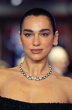 Headshot of Dua Lipa, a young, white woman with dark hair wearing a black outfit