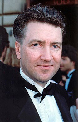 Portrait of David Lynch, a white middle-aged man, with short hair, a shaved beard, fairly aged, greyscale.