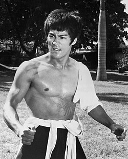 Black-and-white photograph of Lee standing shirtless outdoors
